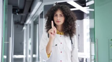 Beyaz önlüklü kadın doktor çapraz kollar, X işareti, modern hastane kliniğinde dururken başını sallıyor. Tıp doktoru bir yasaklama, inkar, anlaşmazlık jesti gösteriyor.