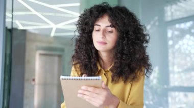 Webcam görüntüsü. Genç bayan çalışan, bir not defterinde video arama eğitimi notlarını izliyor. Bilgisayardaki ekrana bakıyor ve iş yerinde oturuyor. İş kadını internetten ders çalışıyor, öğretmeniyle konuşuyor.