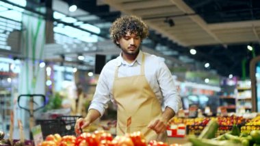 Süpermarkette ya da markette çalışan yakışıklı bir manav ya da küçük bir işletme sahibi marketteki sebze reyonunun yanındaki domatesleri topluyor tezgahın arkasında çalışan genç Latin erkek çalışan