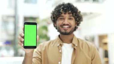 Erkek müşteri, alışveriş merkezi mağazasında ya da havaalanında mobil uygulama uygulaması için yeşil ekran telefon akıllı telefon gösteriyor.