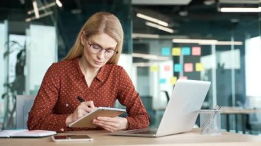 İş kadını internetteki video konferansını izliyor. Not alıyor. Ofiste oturan dizüstü bilgisayar ekranına bakıyor. Uzaktan eğitim, kurs ya da seminer dinleyen kadın çalışanlar