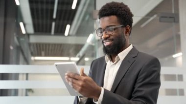 Mutlu Afro-Amerikan iş adamı iş yerinde dijital tablet kullanıyor. Erkek işçi bir başvuru üzerinde çalışır, daktilo, sohbet, bankacılık, sipariş ya da internette gezinme. Kapat.