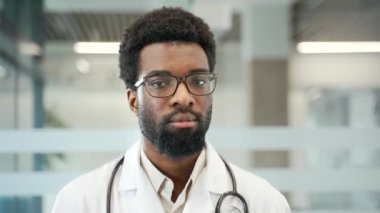 Modern hastanede gözlük ve steteskop takan Afrikalı Amerikalı erkek doktorun portresi. Kendine güvenen ve profesyonel bir tıp çalışanı kameraya bakarak kendini adamış ve odaklanmıştır. Kapat.