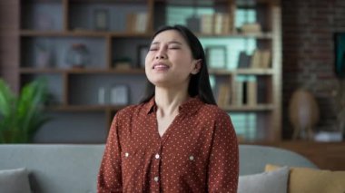 Alerjik Asyalı kadın hapşırır ve burnunu mendille siler. Evdeki oturma odasındaki kanepede oturan, mevsimsel alerjiden muzdarip hasta genç bir kadın. Soğuk algınlığı geçiren bir kız. Kapat.