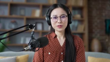 Webcam görüntüsü. Asyalı kendine güvenen bir kadın ofisteki kameraya mikrofon kullanarak podcast yapıyor. Vlogger etkileyicisi çevrimiçi yayın yapıyor, röportaj, webinar, video çağrısı ile uzaktan konuşuyor