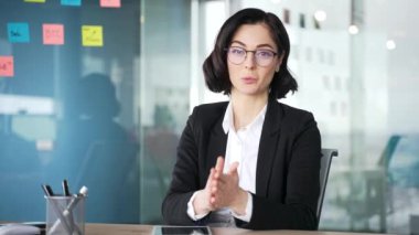Webcam görüntüsü. Kendine güvenen iş kadını, modern ofisteki dizüstü bilgisayarla görüntülü görüşme yapıyor. Kadın profesyonel takım üyeleriyle iş, fikir ve kavramları tartışıyor. Kameraya uzaktan bakıyor.