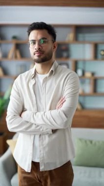 Modern ofis binasında kolları çaprazlanmış, gözlüklü, kendinden emin genç bir adamın portresi. Gömlekli yakışıklı erkek oturma odasında kameraya bakarak poz veriyor. Dikey video