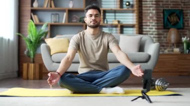 Adam, evdeki oturma odasında yerde yatarken telefonda internet kursu sırasında meditasyon yapıyor. Nilüfer pozisyonunda oturan sakin erkek, video aracılığıyla eğitmeni dinlerken yoga yapıyor.