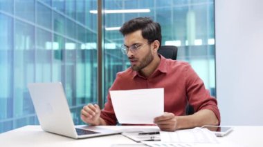 Mali sonuçlardan memnun olmayan kafası karışmış işadamı iş yerindeki bilgisayardaki belgeleri kontrol ediyor. Sinirli erkek muhasebeci, kötü göstergelerle dolu belgeyi okumaktan memnun değil