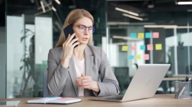 Modern ofiste işyerinde otururken ceketli, cep telefonlu, kendinden emin bir iş kadını konuşuyor. Meşgul bayan yönetici bir ortakla iş konuşur ya da bir müşteriyle sohbet eder.