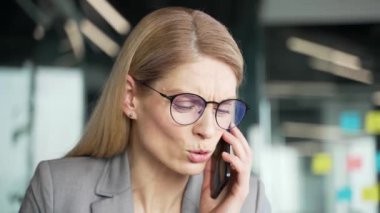 Takım elbiseli kızgın bir iş kadını iş yerindeki iş yerinde cep telefonuyla konuşuyor. İş sorunları, problemler hakkında, akıllı telefondan alt düzey yöneticilerle hayal kırıklığına uğramış kadın kavgaları. Kapat.
