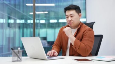 Modern ofisteki dizüstü bilgisayarla ilgili analizler yapan Asyalı işadamı, düşünceli bir profesyonel, masa başında bilgisayarda yazı yazıyor. Erkek girişimci proje üzerinde çalışıyor, iş görevine odaklanıyor