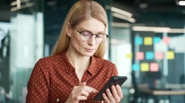 Kendine güvenen iş kadını iş yerinde cep telefonu kullanıyor. Gözlüklü kadın yönetici uygulamada çalışır, bir mesaj yazar, bir istemciyle çevrimiçi sohbet eder veya internette gezinir. Kapat.