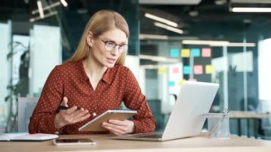 İş kadını internetteki video konferansını izliyor. Not alıyor. Ofiste oturan dizüstü bilgisayara bakıyor. Uzaktan eğitim alan bir kadın ya da özel öğretmenle konuşan bir kurs.