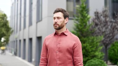 Sakallı işadamı, ofis binasının önünde kolları bağlı duruyor. Doğrudan kameraya bakıyor, profesyonellik ve odaklanma yayıyor. Ciddi bir yöneticinin ya da işçinin kafasından.