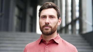 Ofis binasının önünde duran kırmızı gömlekli, güler yüzlü bir iş adamının portresi. Dost canlısı sakallı adam kameraya bakıyor. Mutlu bir patronun, müdürün ya da işçinin vesikalığı.