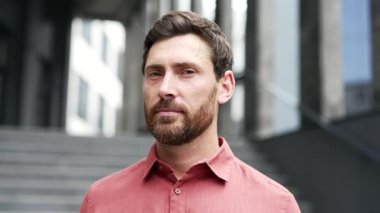 Ofis binasının önünde duran sakallı, kendine güvenen bir girişimci. Şehir ortamında günlük kırmızı gömlek giyen bir iş adamı. Bir adamın portresi. Ciddi bir menajerin kafasından. Kapat.