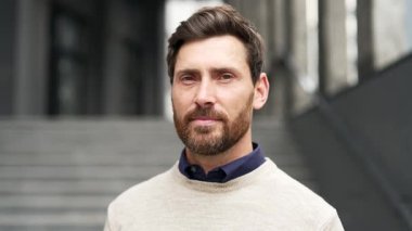 Kendine güvenen gülümseyen bir iş adamının bir ofis binasının önünde duran portresi. Dost canlısı sakallı adam kameraya bakarak poz veriyor. Mutlu bir yönetici ya da öğretmenin vesikalığı.
