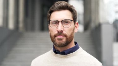 Binanın dışında duran gözlüklü, kendinden emin bir iş adamı. Sakallı adam kameraya ciddi bir ifadeyle bakıyor. Yakışıklı bir adamın portresi. Ciddi bir menajerin kafasından. Kapat.