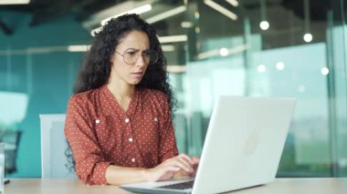 İş yerindeki bir masada dizüstü bilgisayarla çalışırken göz yorgunluğundan muzdarip genç bir iş kadını. Gözlük masajı yapan yorgun bir kadın, parmaklarıyla burun köprüsünü ovuyor.