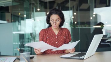 Ofiste çalışırken evrak işleriyle uğraşan genç bir iş kadını hayal kırıklığına uğradı. Şaşkın kadın çalışan belgelere ve kameraya bakıyor ve sorunu anlayamıyor.
