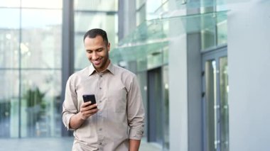 Şehir caddesinde elinde telefonla yürüyen yakışıklı bir iş adamı. Ofis çalışanı erkek işadamı sohbet ediyor. Dışarıdaki ofis binasının yakınında gülümseyen akıllı telefona bakıyor.