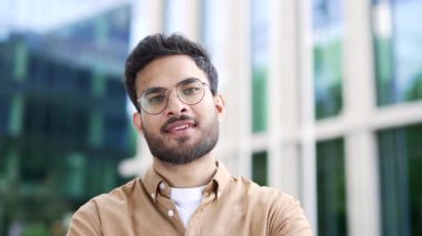 İş yeri binasının yanındaki caddede duran yakışıklı bir işadamının portresi. Gözlüklü, kameraya bakarak gülümseyen sakallı adam. Girişimcinin baş fotoğrafı. Kapat.