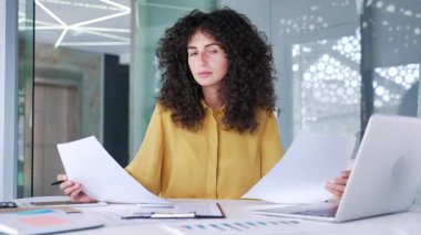 Kafası karışmış bir iş kadını, iş yerindeki masasında otururken evrak işlerinde zorlanıyor. Şaşkın kadın çalışan belgelere bakıyor ve kameraya bakarken sorunu anlayamıyor.