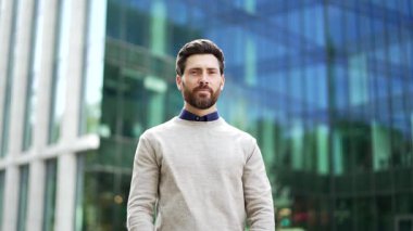 Kendine güvenen iş adamının portresi arka planda modern cam bina ile kentte çapraz kollarla gülümsüyor. Mutlu iş adamı pozitif tavır ve güven gösteriyor. Kameraya bakıyor.