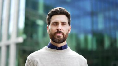 Arka planda modern cam bina ile şehir dışında duran gülümseyen iş adamının portresi. Kendine güvenen yetişkin erkek profesyonel pozitiflik ve iş ortamında başarı. Kapat.