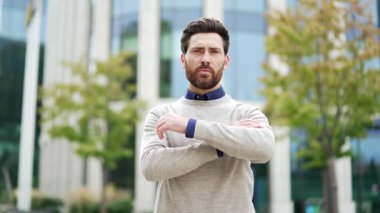 Ciddi bir işadamının portresi, şehir merkezinde kendine güvenle kollarını kavuşturmuş, azim ve profesyonelliği yansıtan bir şekilde duruyor. Olgun erkek liderlik ve başarıyı temsil eder.