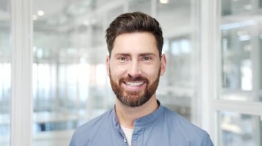 Modern cam iş ofisindeki işyerinde duran gülümseyen iş adamının portresi. Kameraya bakan mutlu, başarılı girişimcinin baş görüntüsü. Çalışma alanında yakışıklı bir yönetici. Kapat.