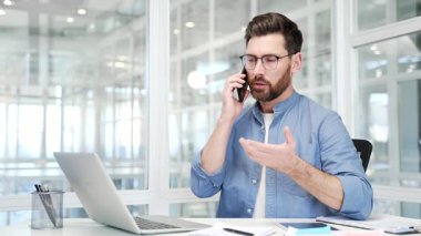 Modern ofisteki çalışma masasında otururken kendine güvenen işadamı cep telefonuyla konuşuyor. Yönetici bir müşteriyle iletişim kurar ya da iş ortağıyla akıllı telefon kullanarak iletişim kurar.