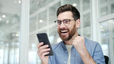 Mutlu iş adamı iş yerindeki iş yerinde cep telefonundan harika haberler aldı. Gülümseyen şaşkın girişimci olumlu iyi bir mesaj okuyor, başarıyı kutluyor. Kapat.