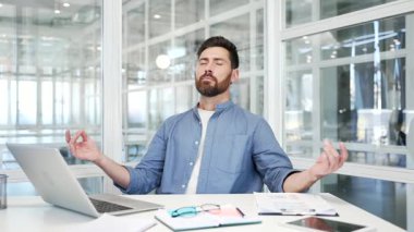 İş adamı, bir iş yerinde iş yerinde otururken kapalı gözlerle meditasyon yapıyor. Sakin yakışıklı işçi yoga yapıyor ve huzuru hissediyor. Erkek stres atmak için rahatlatır.