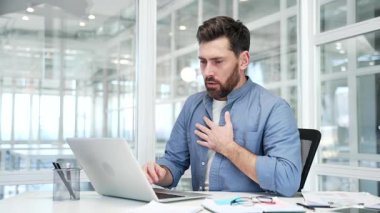 Hasta iş adamı, bir iş yerinde çalışırken dizüstü bilgisayarla kalp krizi geçiriyor. Erkek işçi göğsündeki gerilimden muzdarip ve elleriyle hassas noktayı tutuyor.