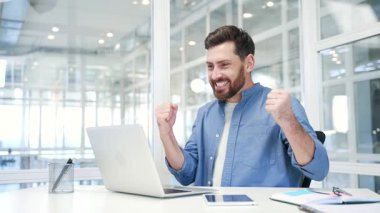 Mutlu iş adamı, modern iş ofisindeki iş yerinde otururken dizüstü bilgisayarından harika haberler aldı. Gülümseyen şaşkın girişimci olumlu bir mesaj okur, başarıyı kutlar