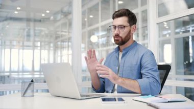 Kendine güvenen bir iş adamı, modern bir ofiste iş yerinde oturan bir dizüstü bilgisayarla video görüşmesinde konuşuyor. Girişimcinin bir iş toplantısı var. Müdür çevrimiçi bir konferansta uzaktan konuşuyor.