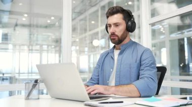Odaklanmış iş adamı ya da kablosuz kulaklık uzmanı bir iş yerindeki bir laptopta çalışır. Ciddi kodlayıcı geliştirici programlıyor, bilgisayardaki bir projeyle meşgul