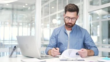 Kendine güvenen işadamı, iş yerindeki bir masada oturan belgeleri imzalıyor. Gözlüklü yönetici dosyasına bakar, belgeleri kontrol eder ve sözleşmeyi kalemle imzalar.