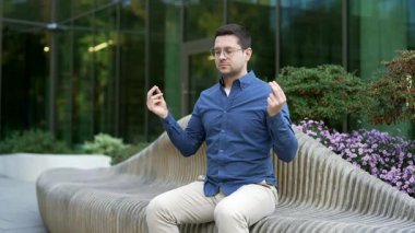 İş adamı, kapalı gözlerle meditasyon yapıyor. İş yerinin yanındaki bankta oturuyor. Yakışıklı erkek işçi derin nefes alma yogası yapar. Sakin adam stresi azaltır, huzuru hisseder.