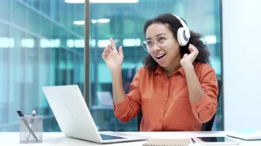 Modern iş yerlerinde müzik dinleyen, kablosuz kulaklık takan mutlu, Afro-Amerikan iş kadını. Gülümseyen siyah kadın dans ederken şarkının tadını çıkarıyor