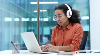Genç Afro-Amerikan kadın bilişim uzmanı. Kulaklık uzmanı. İş yerindeki laptopta oturuyor. Odaklanmış siyah kadın geliştirici podcast dinlerken bilgisayarda çalışıyor