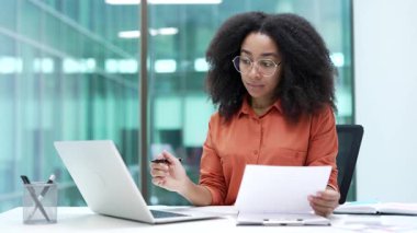 Meşgul Afro-Amerikalı iş kadını iş yerindeki bir bilgisayarla evrak işleriyle uğraşıyor. Odaklanmış kadın finansör mali raporlarla ilgileniyor, muhasebe ile meşgul.