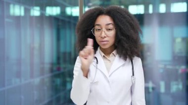 Afro-amerikan kadın doktor kollarını çapraz gösteriyor, X işareti, baş ve parmak sallama hastane kliniğinde durmuyor. Tıp doktoru yasaklama, inkar, anlaşmazlık jesti gösteriyor.