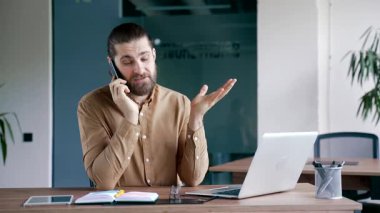 Modern ofisteki çalışma masasında otururken kendine güvenen işadamı cep telefonuyla konuşuyor. Yönetici bir müşteriyle iletişim kurar ya da iş ortağıyla akıllı telefon kullanarak iletişim kurar.