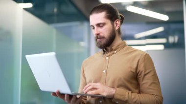 Gülümseyen bir bilişim mühendisinin portresi veri merkezinin iş ofisinde duran bir dizüstü bilgisayarda çalışıyor. Güvenilir müteahhit teknisyen iş adamı poz veriyor ve kameraya bakıyor. Kapat.