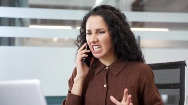 Ofiste cep telefonuyla konuşan kızgın bir iş kadını. Hüsrana uğramış kadın yönetici duygularını ifade ediyor, stresli iş durumuyla ya da çatışma çözümleriyle uğraşıyor. Kapat.