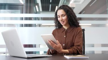 Modern iş ofisindeki iş yerinde dijital tablet ve dizüstü bilgisayar kullanan genç bir iş kadını. Kadın çalışan proje üzerinde çalışıyor, internette gezinme, daktilo veya bankacılık gibi görevlere katılıyor