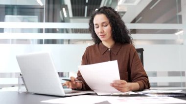 İş yerindeki mali sonuçlardan memnun olan mutlu bir iş kadını. Gülümseyen kadın finansör belgelere ve bilgisayar ekranına bakıyor, olumlu göstergelere seviniyor, başarı